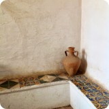 A stairwell vignette of old Spanish tile and pottery with white-washed walls bathed in shifting sunlight.